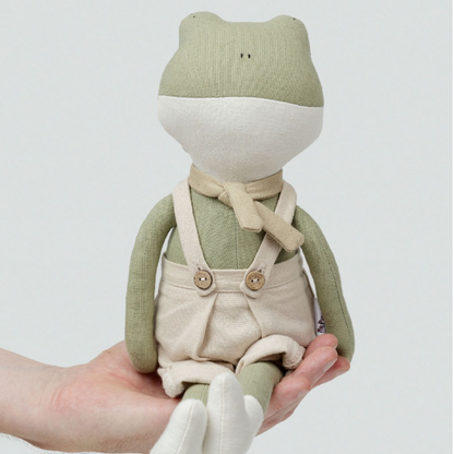 frank the Frog wearing overalls held in a hand against a white background